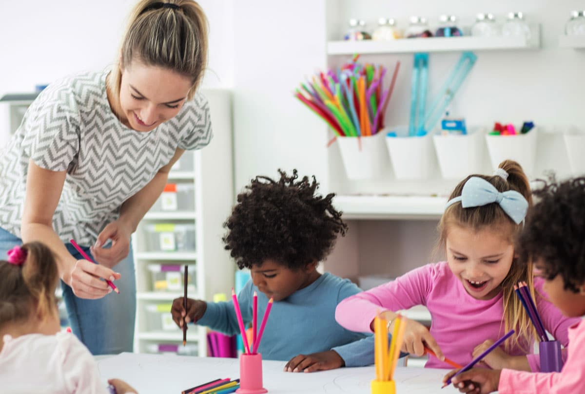 Diverse toddlers learning to write by the help of their teacher at a preschool & child care center Serving Smithfield, RI.